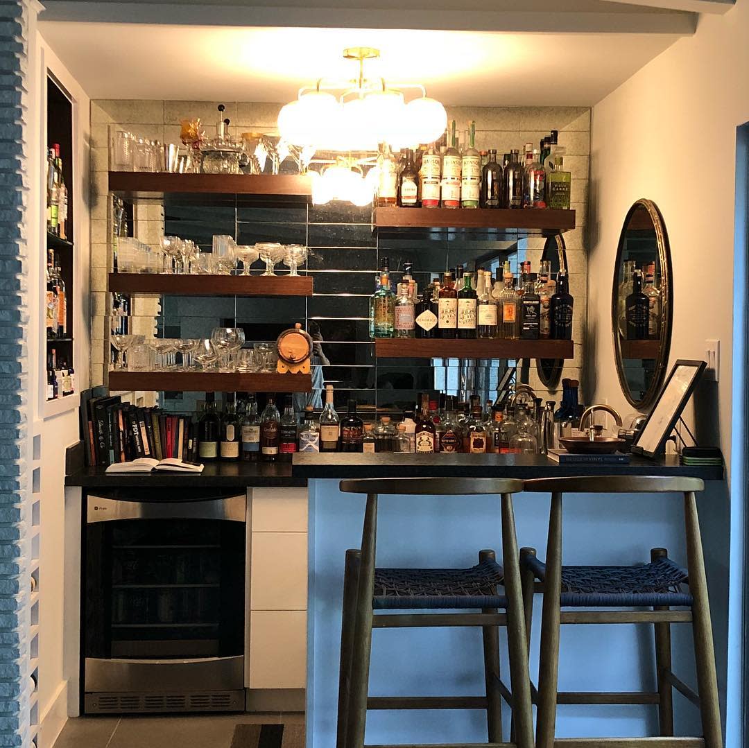 Fully stocked home bar with wooden shelves, glassware, liquor bottles, and a small fridge.